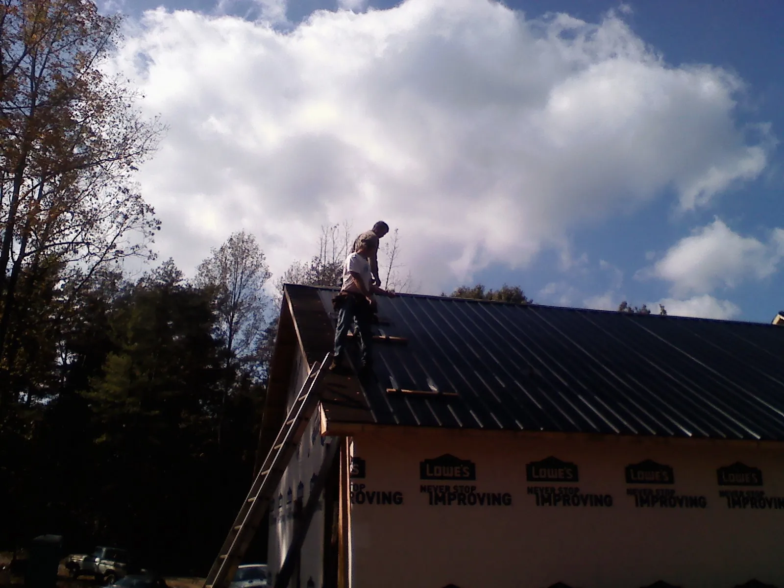 Roofer fastening dark metal panels high against a cloudy sky, from a Roof Inspection job in Covington